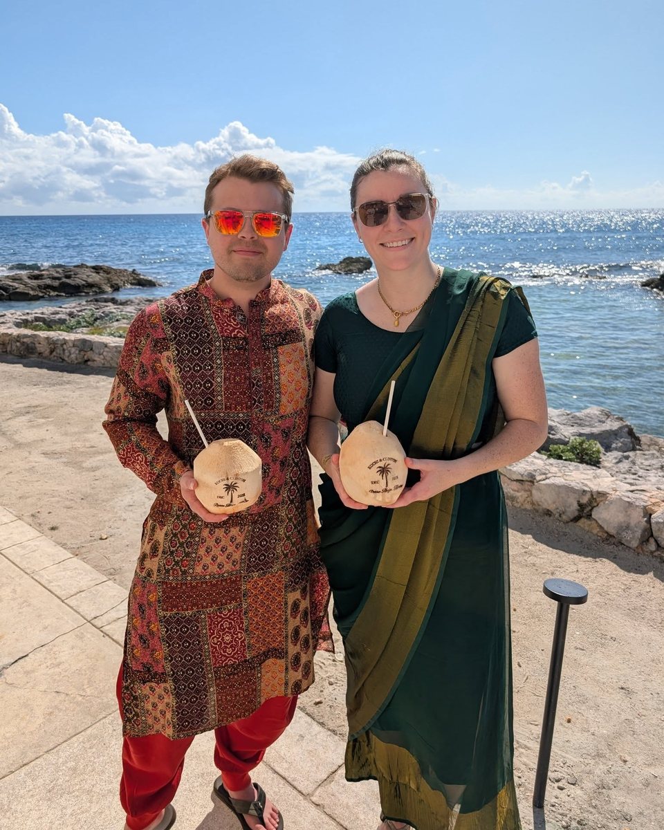 Todd Reboul and Hannah by the ocean, each holding a coconut